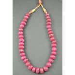 An Indian ruby necklace, comprising thirty seven carved beads hanging on red and gold cord.