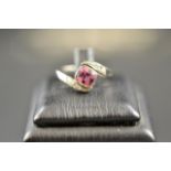 A white metal cross-over style ring with square pink sapphire and diamond set shoulders - size P.