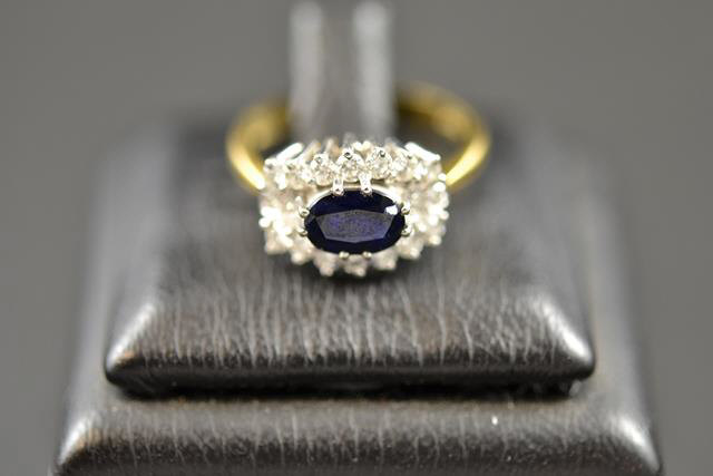 An 18ct gold ring with central sapphire surrounded by eighteen diamonds in cluster setting - size M.