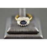 An 18ct gold ring with central sapphire surrounded by eighteen diamonds in cluster setting - size M.