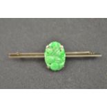 A platinum bar brooch, mounted with jade with carved and pierced foliate decoration - L 5.5cm.