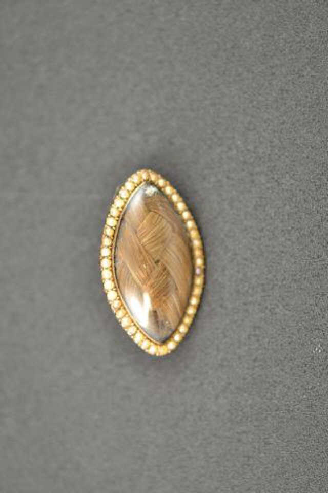 A marquise shaped yellow metal mourning brooch mounted with plaited hair bordered by pearls -