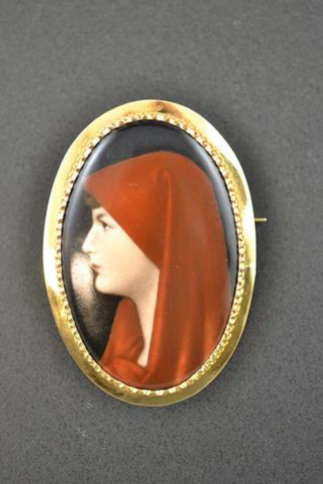 A gold brooch mounted with hand painted porcelain plaque depicting girl in red headscarf, 'pie-