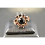 A 9ct gold ring with central garnet surrounded by ten smaller garnets in floral setting - size P.