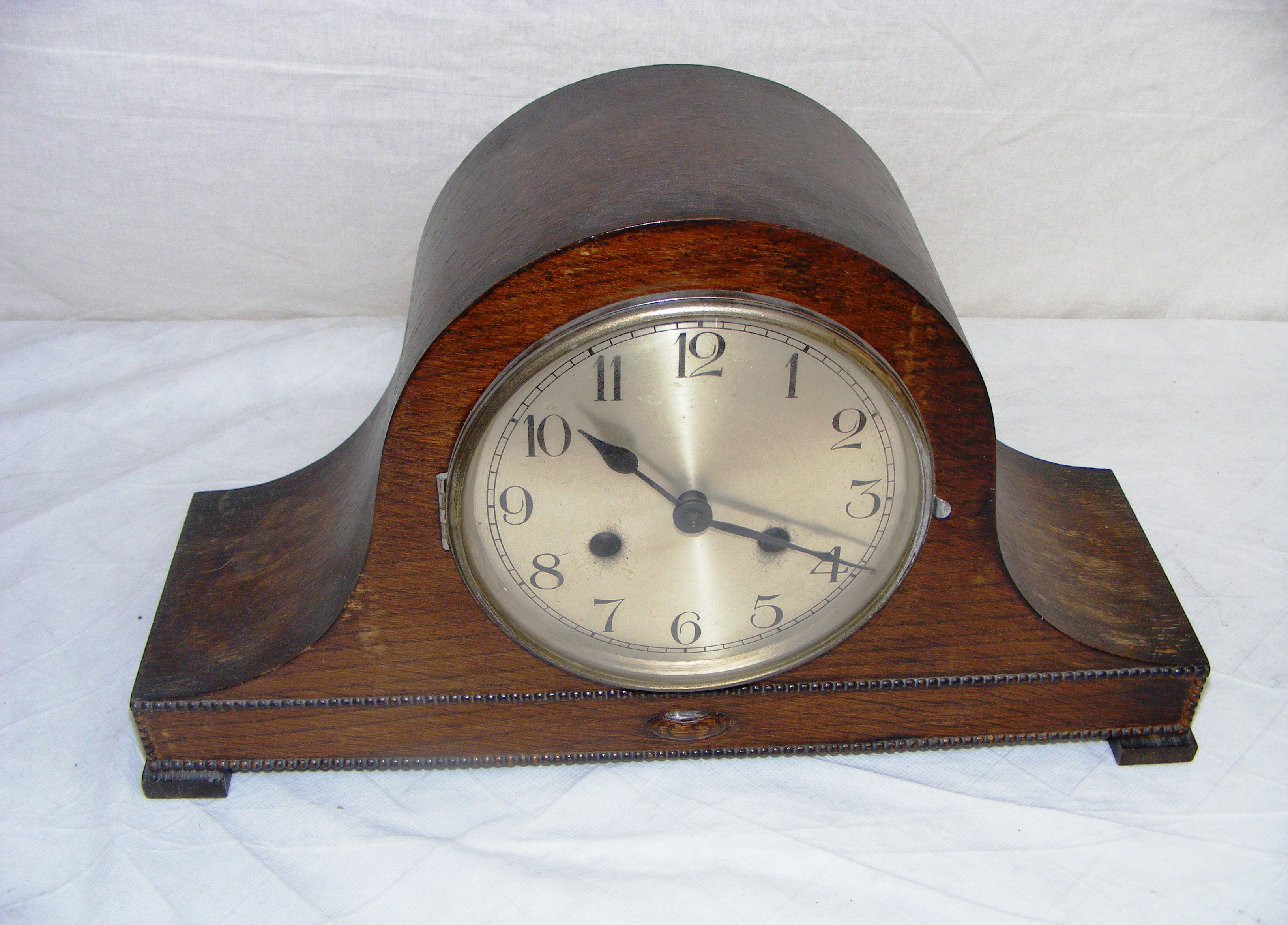 An oak mantle clock in the "Napoleon Hat" shape, appears to be in a ticking order, but comes without