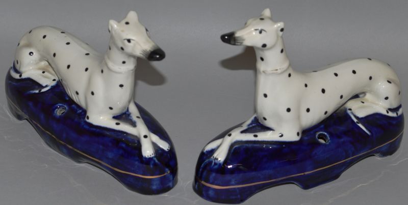 A PAIR OF STAFFORDSHIRE LAYING GREYHOUNDS, WHITE WITH BLACK SPOTS, gilt collar, lying cross legged