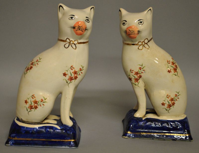 A PAIR OF FLORAL DECORATED STAFFORDSHIRE CATS with gilt ribbon collar, orange nose on blue gilt