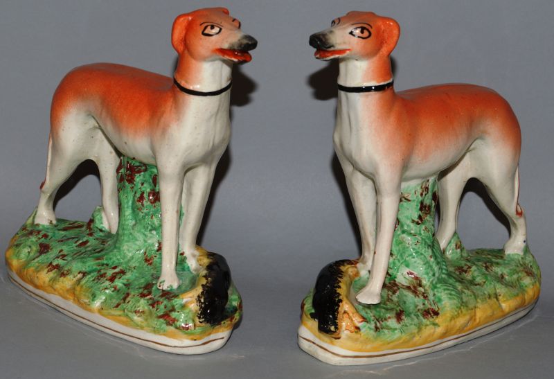 A PAIR OF STAFFORDSHIRE STANDING GREYHOUNDS, standing on rustic bases with a dead rabbit. 6.5ins