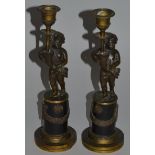 A PAIR OF 19TH CENTURY BRONZE CUPID CANDLESTICKS holding cornucopia urns and standing on plinths.