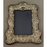 AN UPRIGHT EASEL PHOTOGRAPH FRAME WITH REPOUSSÉ DECORATION with scrolls and cupids. 9ins high x 7ins