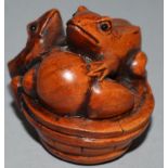 A CARVED WOOD NETSUKE, three toads on a barrel.