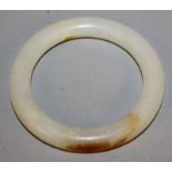 A CHINESE WHITE JADE-LIKE BANGLE, the stone with brown inclusions, 3.1in diameter, the inner rim 2.