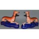 A PAIR OF STAFFORDSHIRE LAYING GREYHOUNDS cross legged on blue gilt lined bases with pen holders.