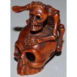 A BOXWOOD NETSUKE, A SKELETON ON A SKULL, signed.