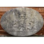 A RECONSTITUTED STONE OVAL PLAQUE, cast in relief depicting cherubs. 2ft 8ins high.