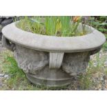 A RECONSTITUTED STONE CIRCULAR GARDEN URN with four strap work handles. 1ft 2ins high.