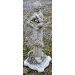 A RECONSTITUTED STONE GARDEN ORNAMENT modelled as a boy playing pipes, seated on a column. 2ft 11ins