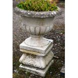 A RECONSTITUTED STONE PEDESTAL URN on shaped, square base. 2ft 9ins high.