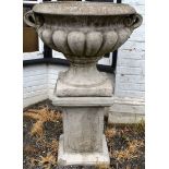 A RECONSTITUTED STONE TWIN HANDLED PEDESTAL URN of lobed design, on a plinth base. 3ft 10ins high.