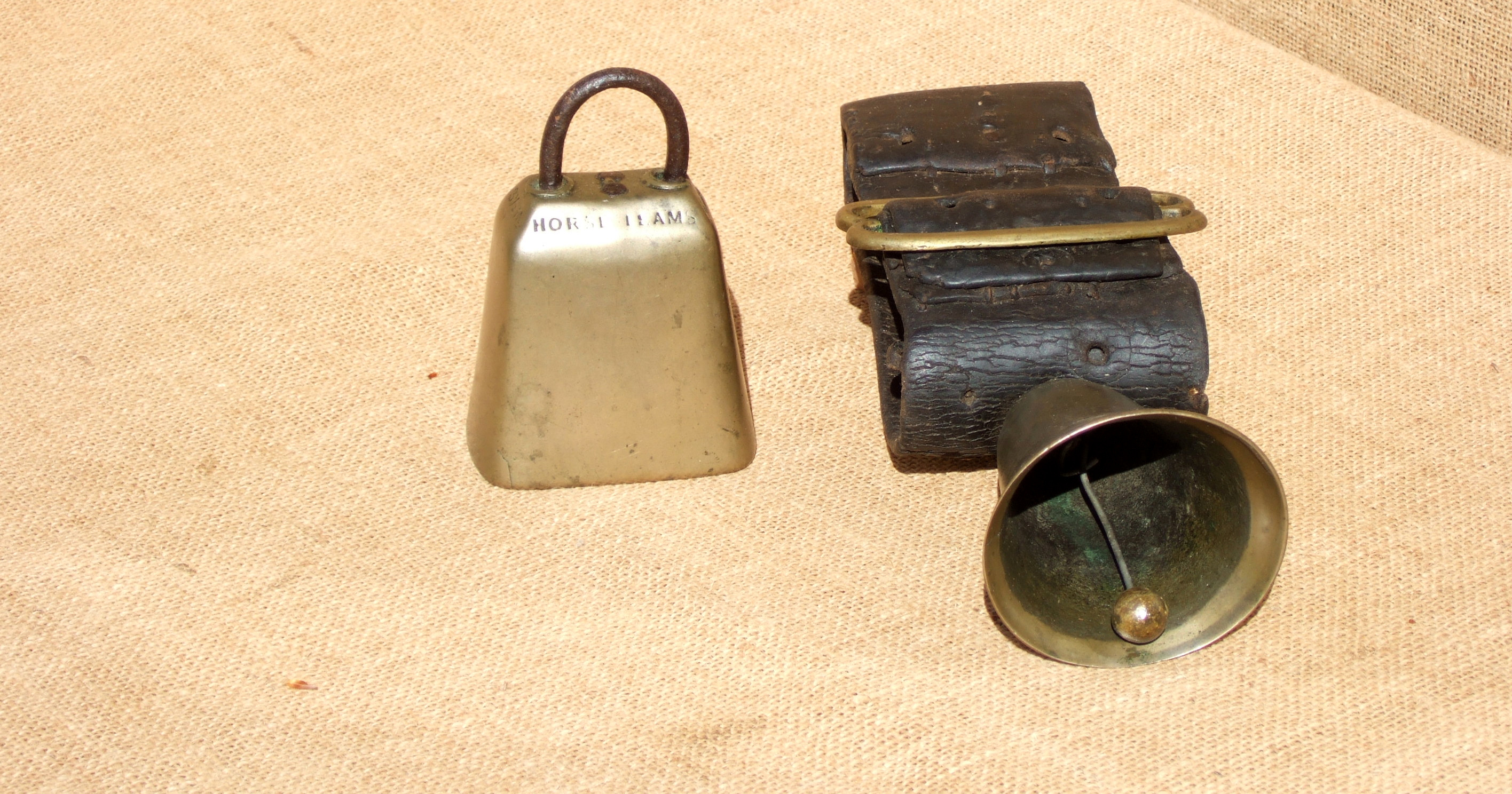 A LATTEN HORSE BELL AND AN ENGRAVED BRASS HORSE BELL. The latten is on a broad brass-buckled