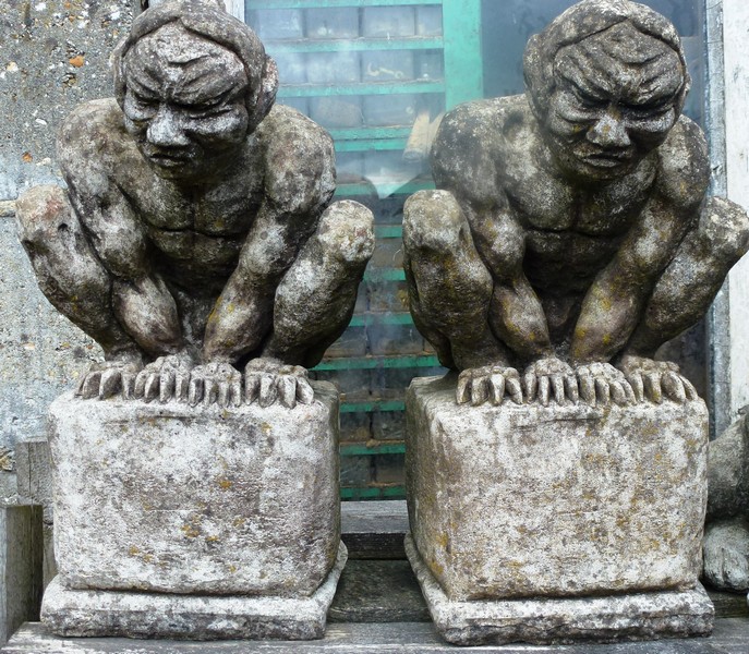 A PAIR OF RECONSTITUTED STONE GARDEN ORNAMENTS “Guardians” on pedestal bases 1ft 3ins high.