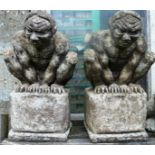 A PAIR OF RECONSTITUTED STONE GARDEN ORNAMENTS “Guardians” on pedestal bases 1ft 3ins high.