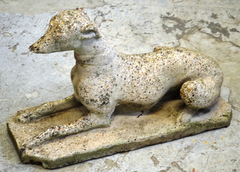 A RECONSTITUTED STONE GARDEN ORNAMENT modelled as a recumbent  dog 2ft 4ins long.