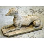 A RECONSTITUTED STONE GARDEN ORNAMENT modelled as a recumbent  dog 2ft 4ins long.