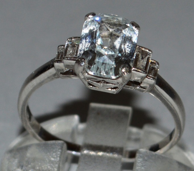 A GOOD WHITE SAPPHIRE AND DIAMOND RING set in platinum, baguette cut central white sapphire with