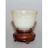 A SMALL 19TH/20TH CENTURY WHITE JADEITE CUP, together with a fitted wood stand, 2.25in high overall,