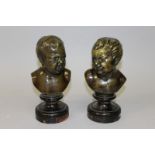 A PAIR OF FRENCH BRONZE CHUBBY CUPID BUSTS on circular wooden bases 8ins high.