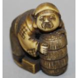 A 19TH/20TH CENTURY JAPANESE STAINED IVORY NETSUKE OF DAIKOKU, leaning forward on a bale, 1.6in wide