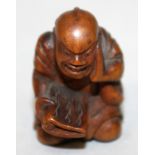 A 19TH/20TH CENTURY JAPANESE CARVED WOOD NETSUKE OF A KNEELING MAN, with demonic expression, holding