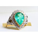 An 18ct gold dress ring set central pear cut emerald with diamond surround and shoulders