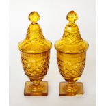 A pair of Regency amber glass sweetmeat jars and covers decorated diamond cutting on square bases (