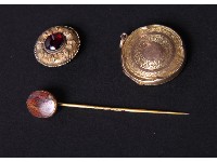 An engine turned circular gold locket, a hardstone mounted stick pin and a yellow metal brooch