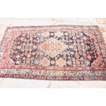 A Persian carpet decorated stylised flowers and central lozenge medallion on a dark blue ground with