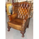 A pair of Georgian design high wing back armchairs, upholstered in brown nailed leather, on carved