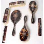 A silver and tortoiseshell seven-piece dressing table set with pique decoration comprising hand