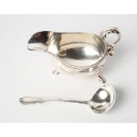 A silver sauce boat with gadrooned border and scrolled handle on three hoof feet and a matching