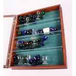 A glazed wall mounted display case containing a collection of coloured glass eye baths, twenty-