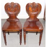 A pair of Victorian mahogany hall chairs with carved backs inset painted armorial of the Clayton