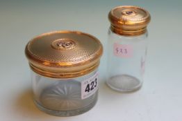 TWO 9CT.GOLD MOUNTED GLASS VANITY JARS WITH ENGINE TURNED DECORATIONS AND BEARING THE LETTER E.   £