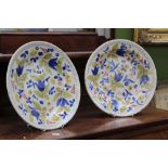 A pair of 19th Century tin glaze plates, decorated with blue, yellow and pink designs, 31cm