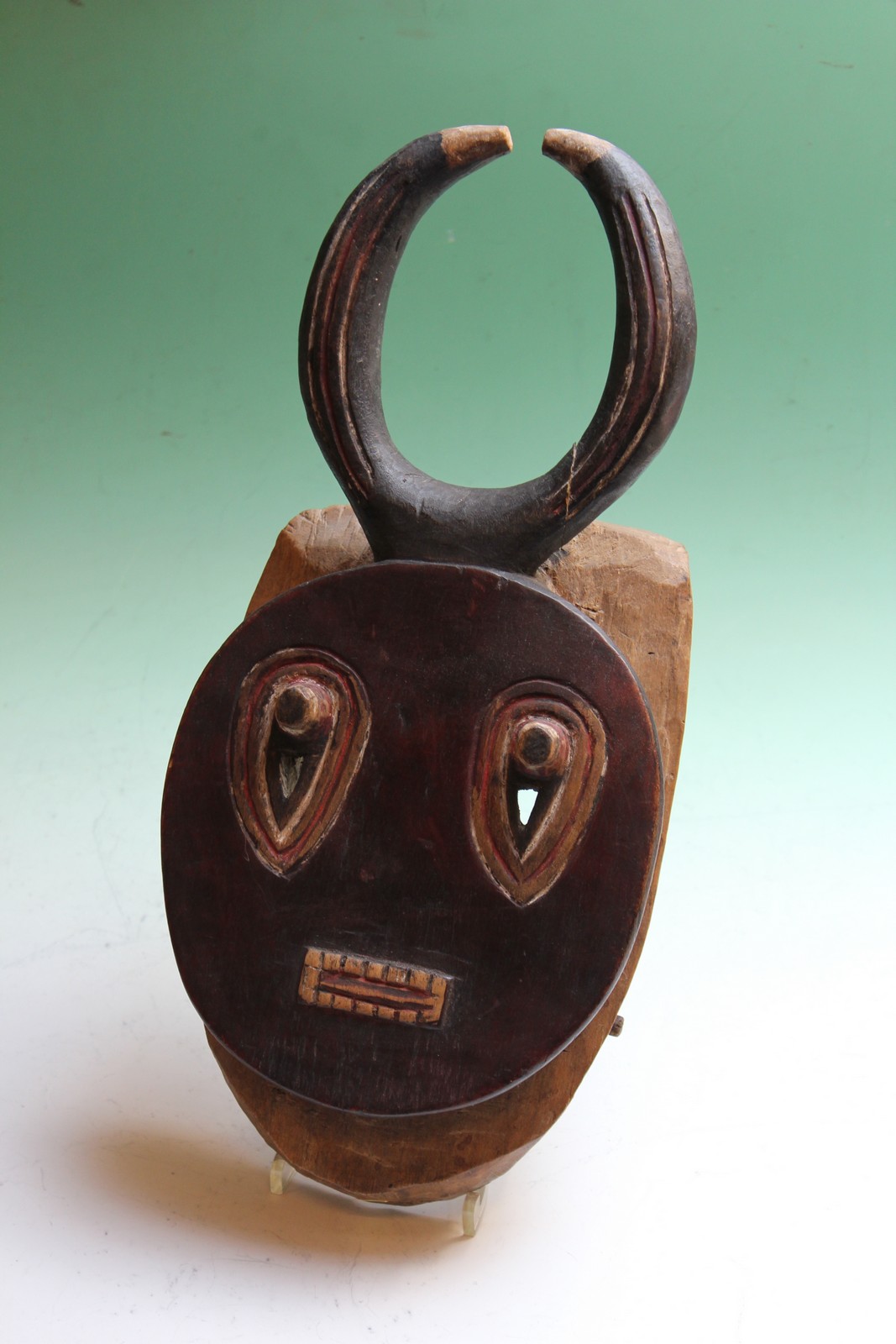 A carved and polychrome tribal ceremonial mask with horn crest, possibly African.