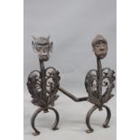A pair of antique iron fire dogs, with leaf and mask decoration