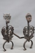 A pair of antique iron fire dogs, with leaf and mask decoration