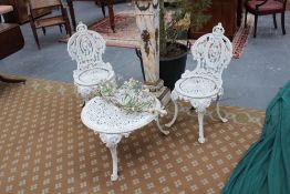 An antique white painted cast iron three piece garden set, comprising a low circular table and two