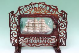 An early 20th Century Folk Art hand made ship in a bottle. Mounted in fret cut table stand with
