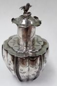 A Chinese silver coloured metal lidded tea canister of lobed form with song bird finial to lid.